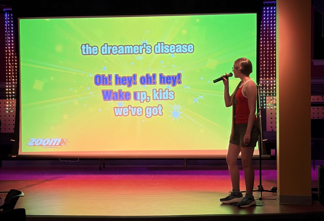 A student stands in front of a big screen singing karaoke