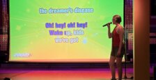 A student stands in front of a big screen singing karaoke