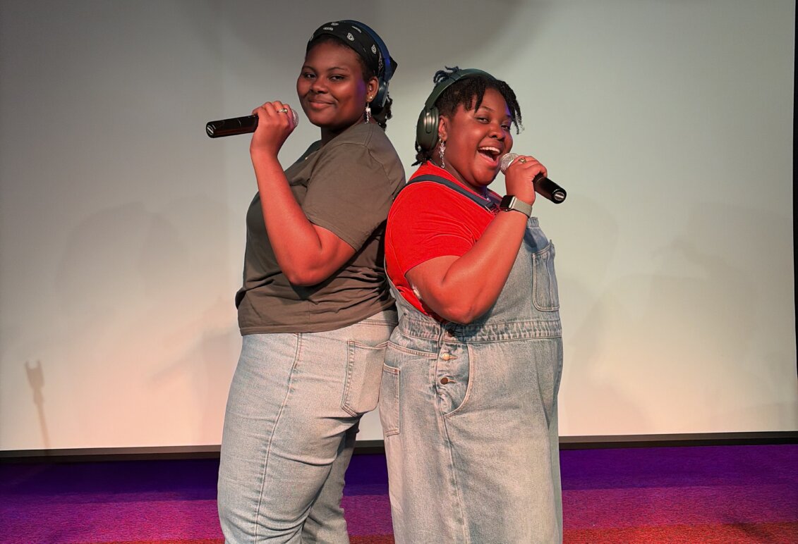 Two students stand back-to-back with microphones