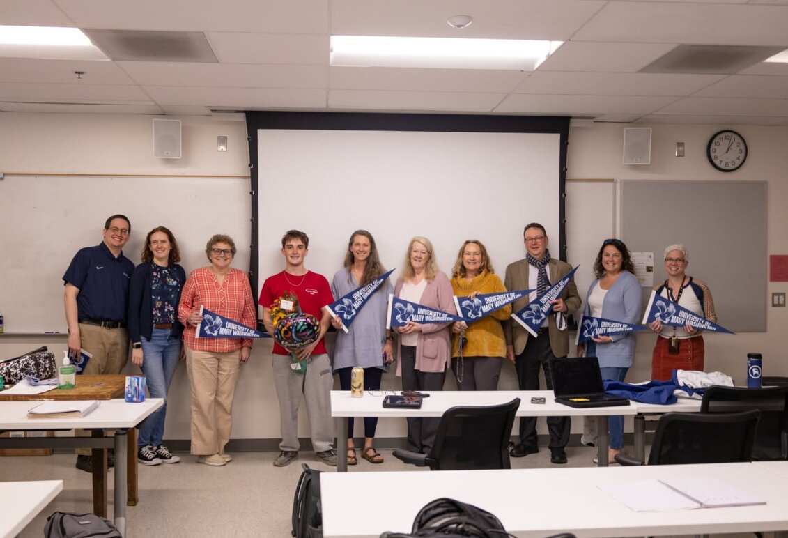Student poses with professors in classroom  