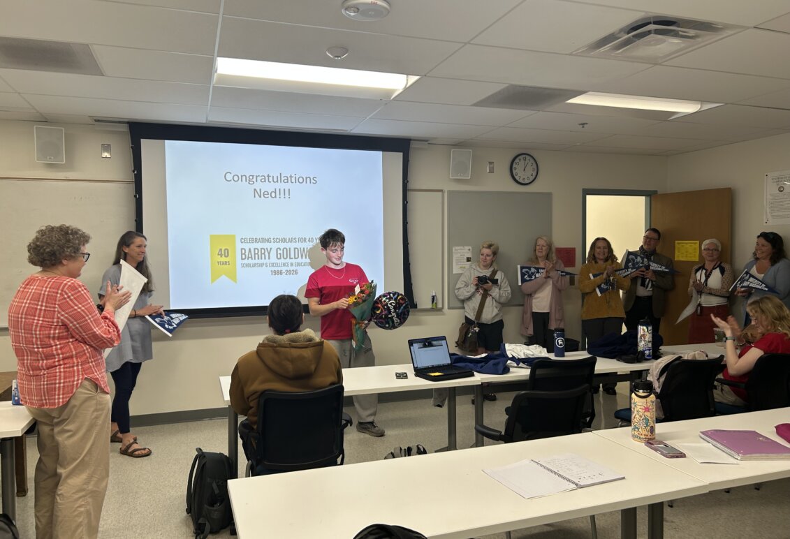 Student receives flowers at the front of a classroom with professors  