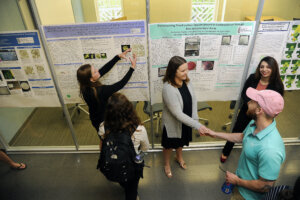 students stand in front of posters talking with others about their projects