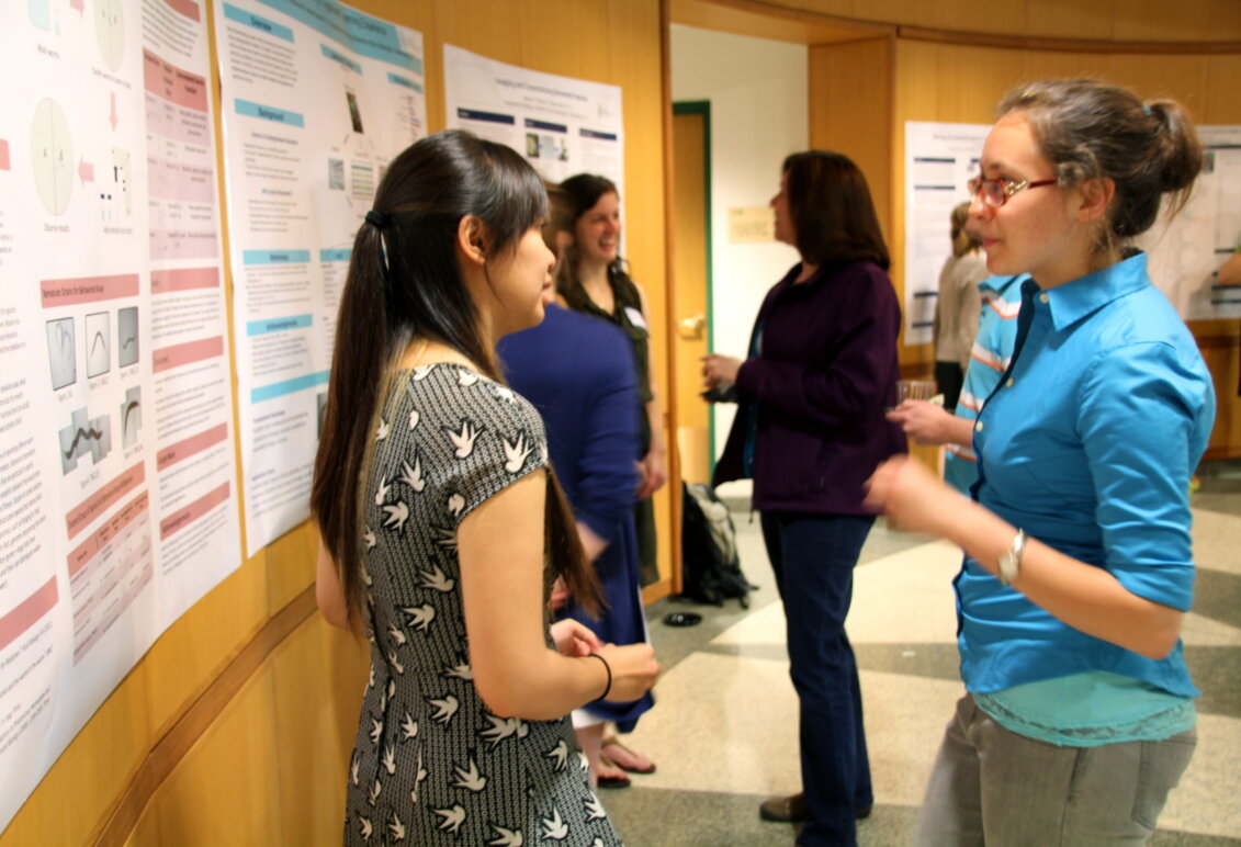 A student stands in front of a poster talking to someone about her research