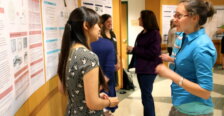 A student stands in front of a poster talking to someone about her research