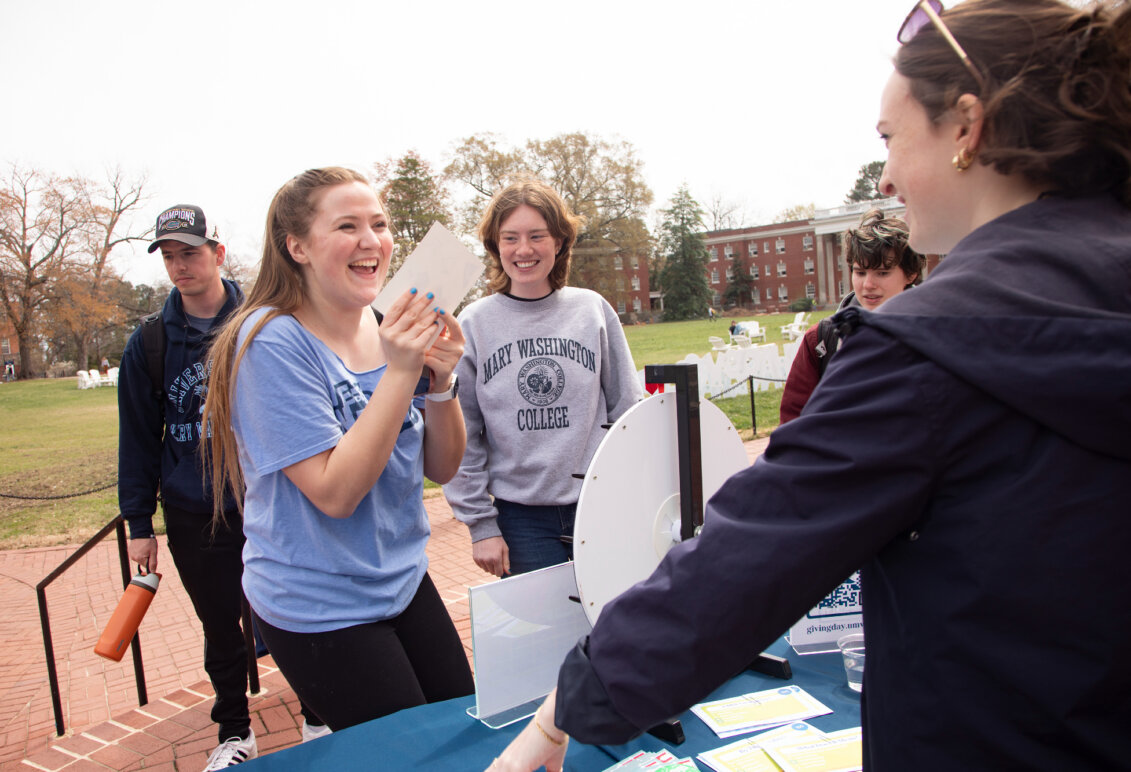 A student spins a wheel while interacting with a volunteer while two others look on.