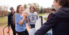 A student spins a wheel while interacting with a volunteer while two others look on.