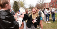 A student pies a volunteer in the face while onlookers have fun in the background.