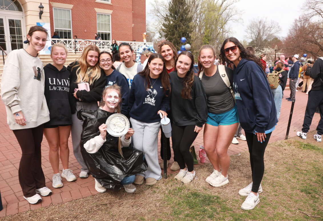A group of UMW women's lacrosse players holding a pie. One is wearing a plastic bag and has just been pied in the face.