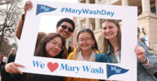 A group of four students in front of the Cedric Rucker University Center holding up a frame that reads #MaryWashDay and We love Mary Wash.