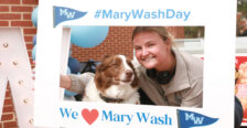 A student and her dog pose for a picture with a sign that says #MaryWashDay and We love Mary Wash.
