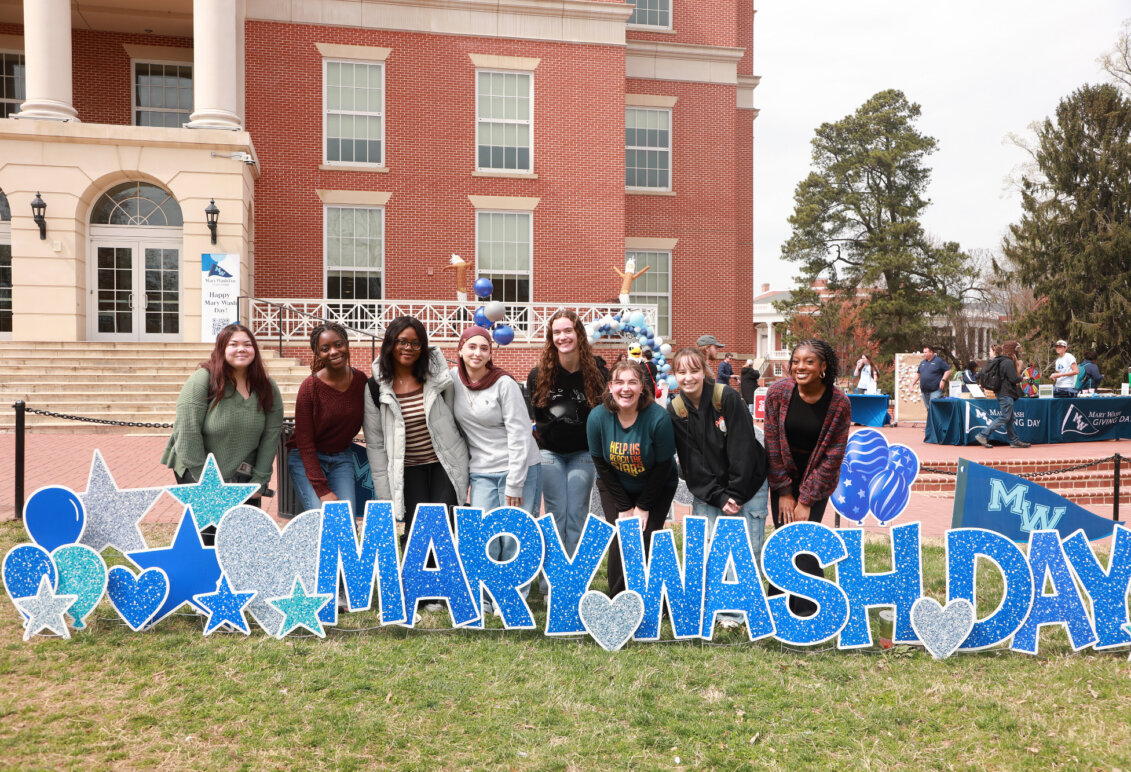 A group of students standing behind the Mary Wash Day sign in front of the Cedric Rucker University Center.