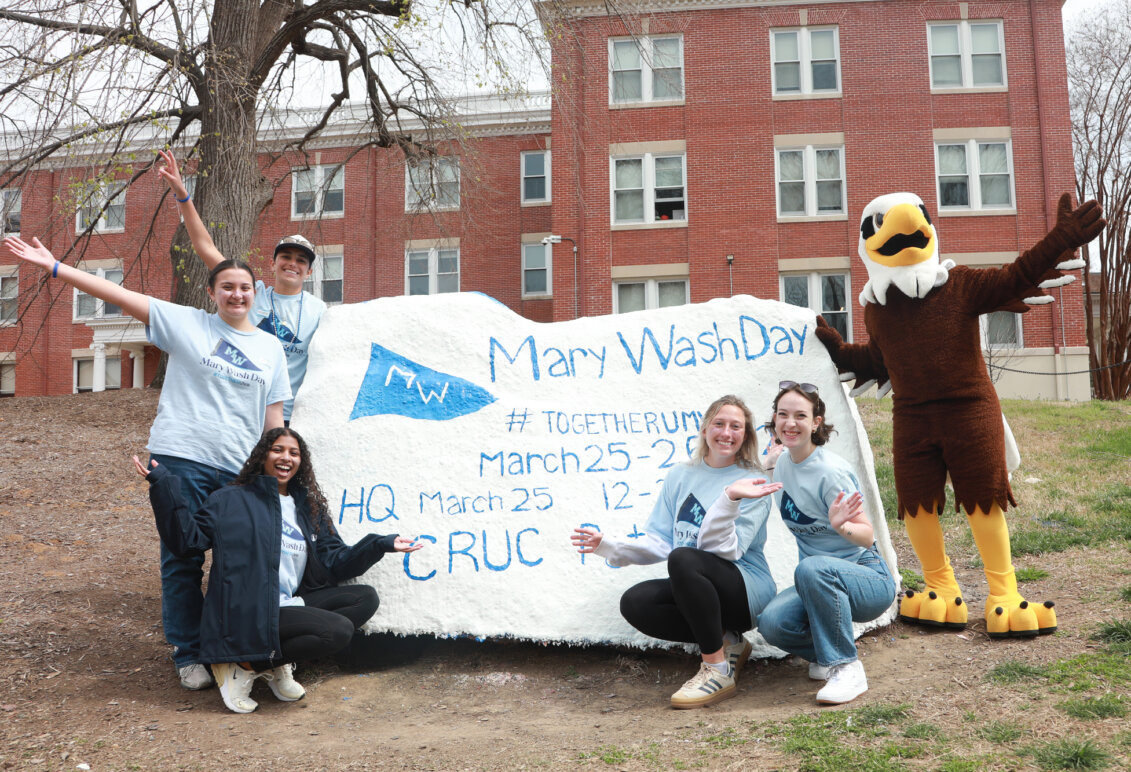 Students with the Spirit Rock that has information about Mary Wash Day. UMW mascot Sammy D. Eagle stands on the right.