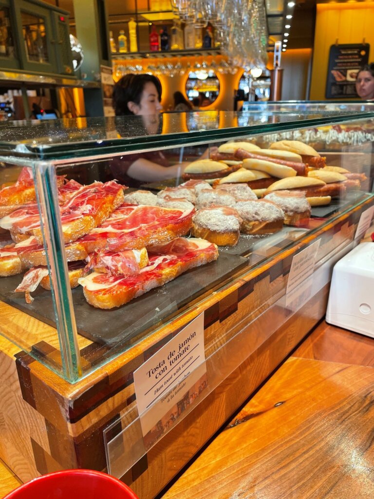 Pintxos inside a counter at a restaurant in Spain. A woman stands behind the counter working in the background.