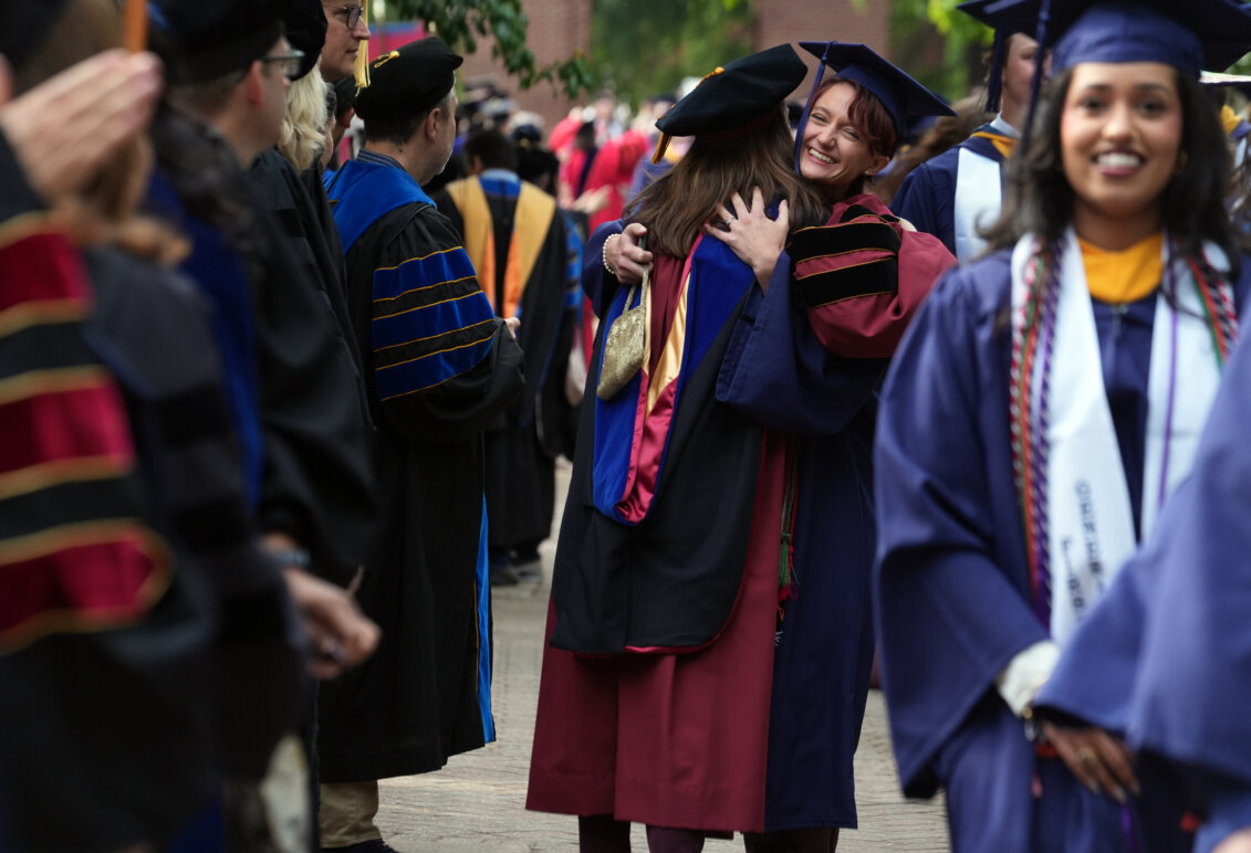 Several people dressed in graduation garb, with two women in the center hugging