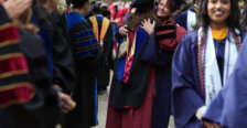 Several people dressed in graduation garb, with two women in the center hugging