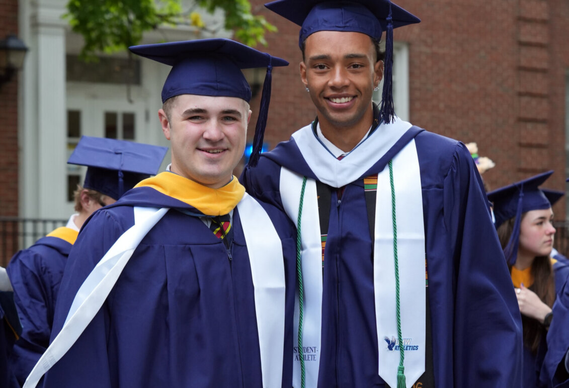 Two guys stand beside each other wearing graduation garb