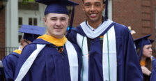 Two guys stand beside each other wearing graduation garb