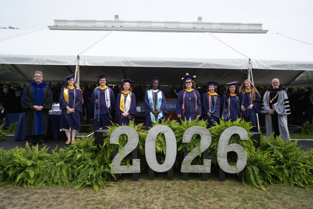 Several people stand in a row looking at the camera and dressed in graduation garb with the number "2026" in front of them