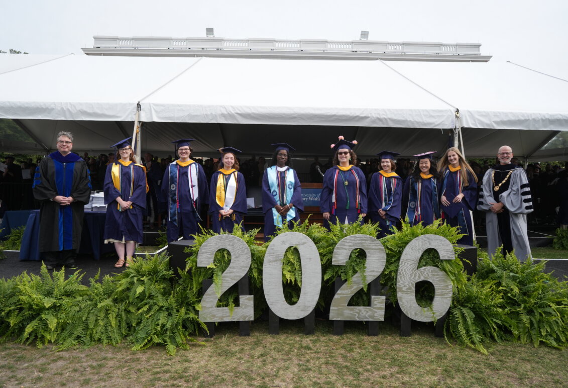 Several people stand in a row looking at the camera and dressed in graduation garb with the number "2026" in front of them