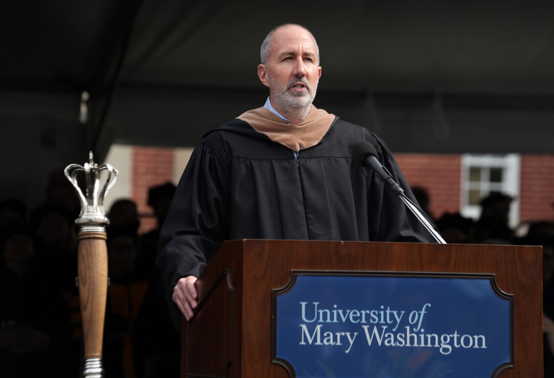 A man dressed in graduation garb stands behind a podium