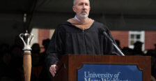 A man dressed in graduation garb stands behind a podium