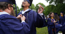Two guys dressed in graduation garb, with one of them helping adjust the other's cords