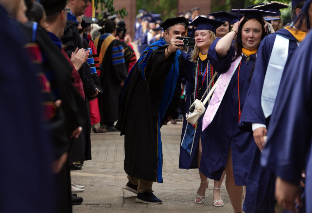 Two people dressed in graduation garb take a selfie