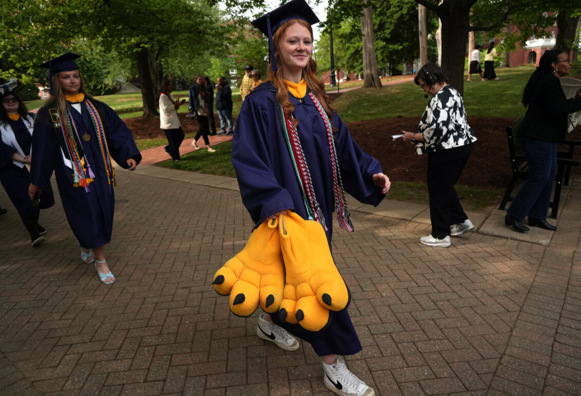 A student dressed in graduation garb carries big bird feet designed for a team mascot