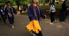 A student dressed in graduation garb carries big bird feet designed for a team mascot