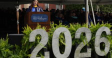 A girl dressed in graduation garb stands behind a podium with the number "2026" in the foreground