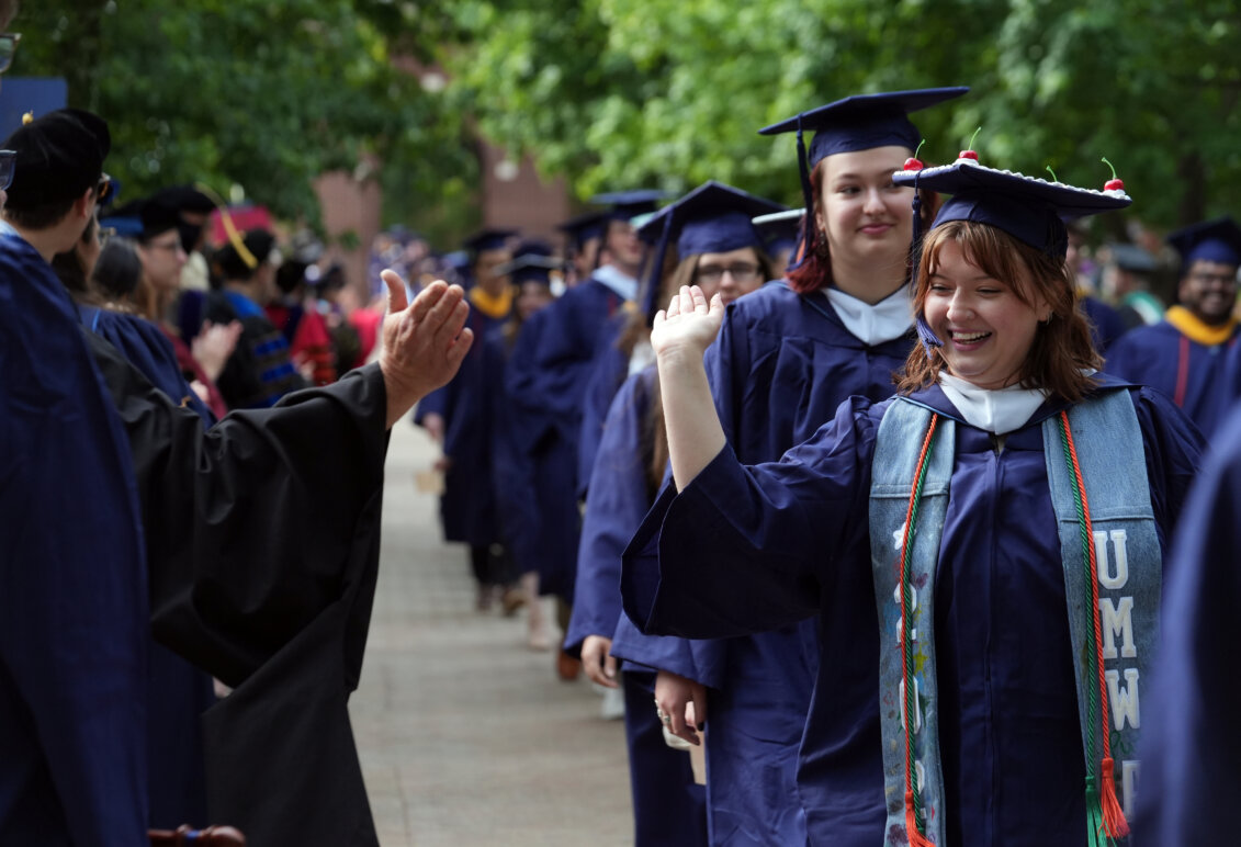 People dressed in graduation garb prepare to give each other a high-five