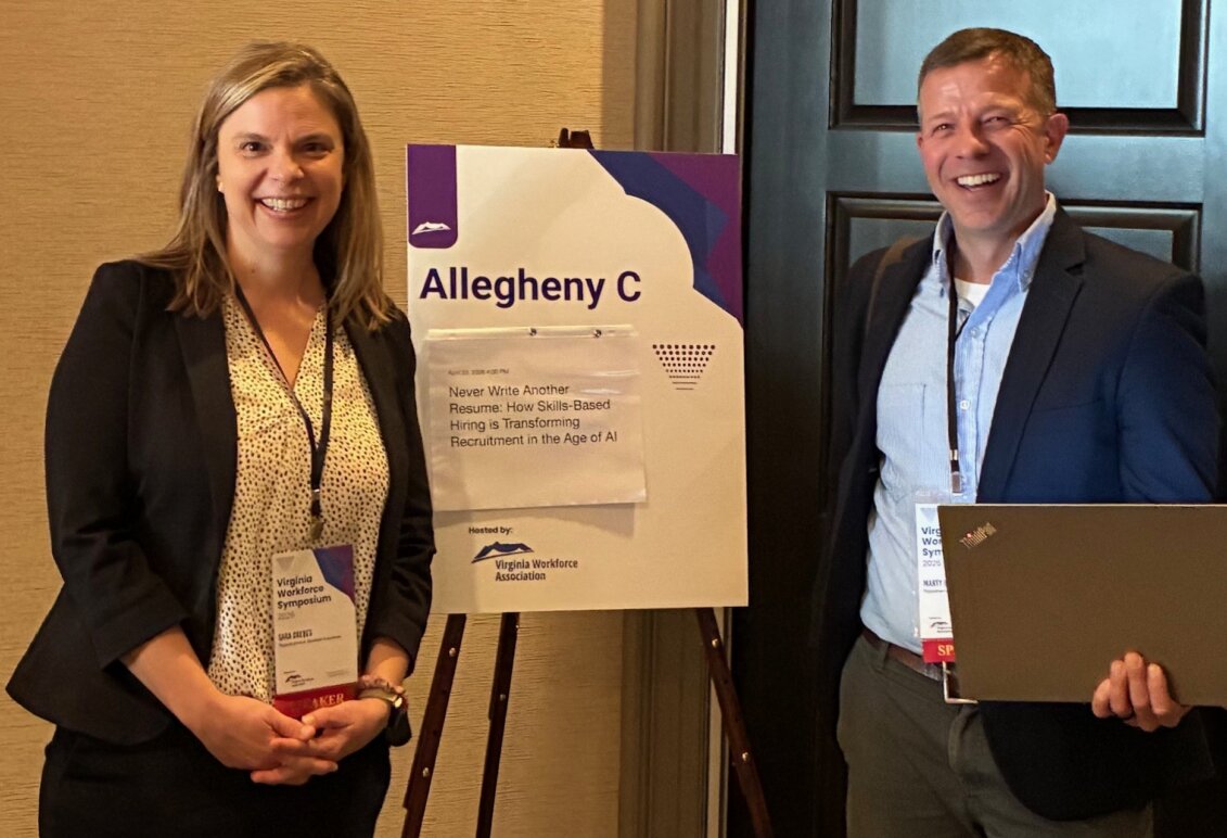 Marty Bywaters-Baldwin poses with a female colleague next to a sign advertising his session at a statewide symposium