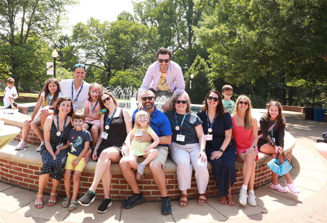 Alumni with their kids, several of whom have painted faces, seated at the fountain in front of Monroe Hall during Reunion Weekend.