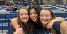 Three women smiling together in the Ron Rosner arena on campus