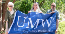 Three Mary Washington alumni hold a UMW flag at the Jepson Alumni Executive Center.