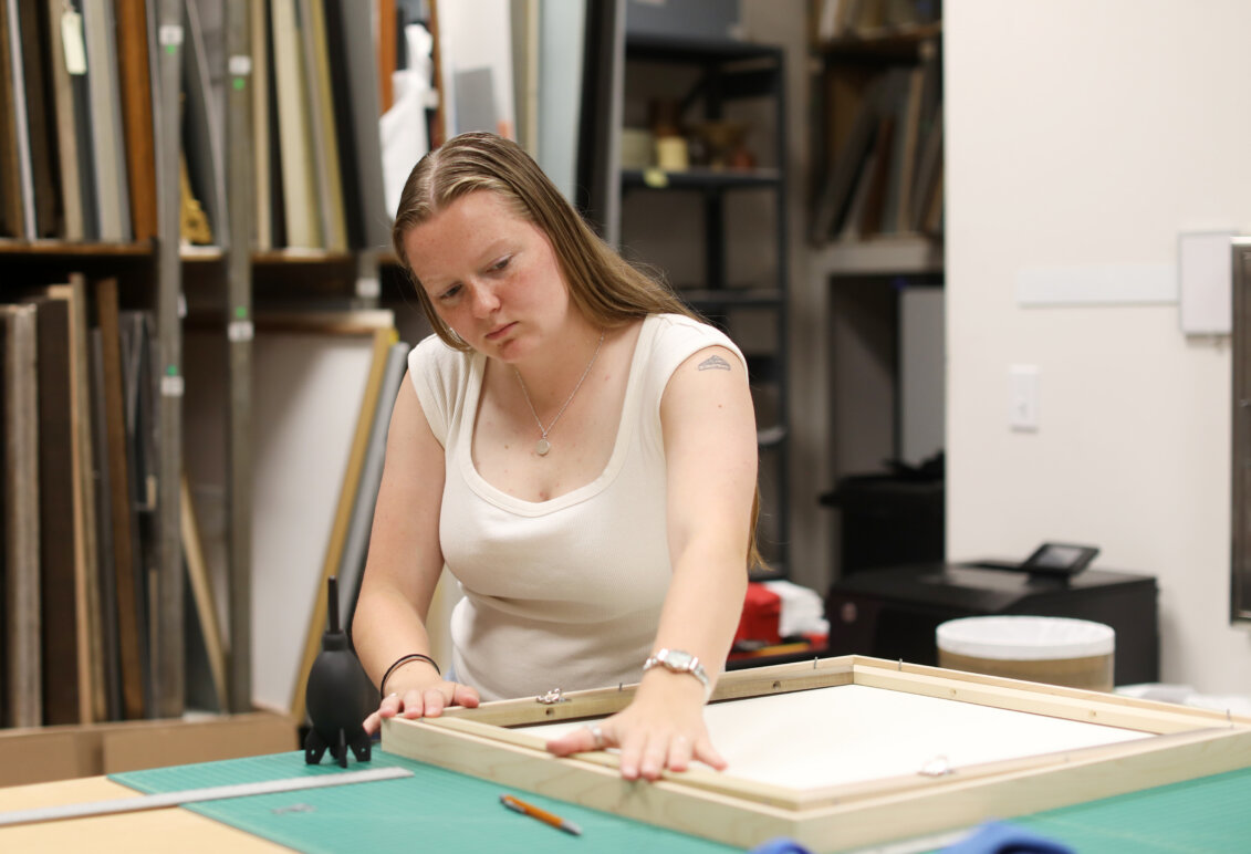 A student works on framing a painting inside an art gallery.