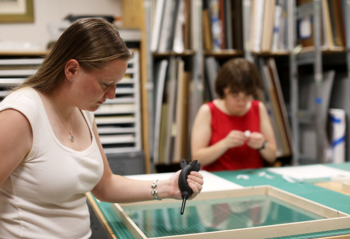 Two students work on processing and framing art inside a studio workspace.