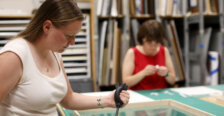 Two students work on processing and framing art inside a studio workspace.