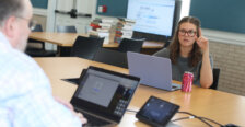 A student sits across the table from a professor, while they are both on their laptops.