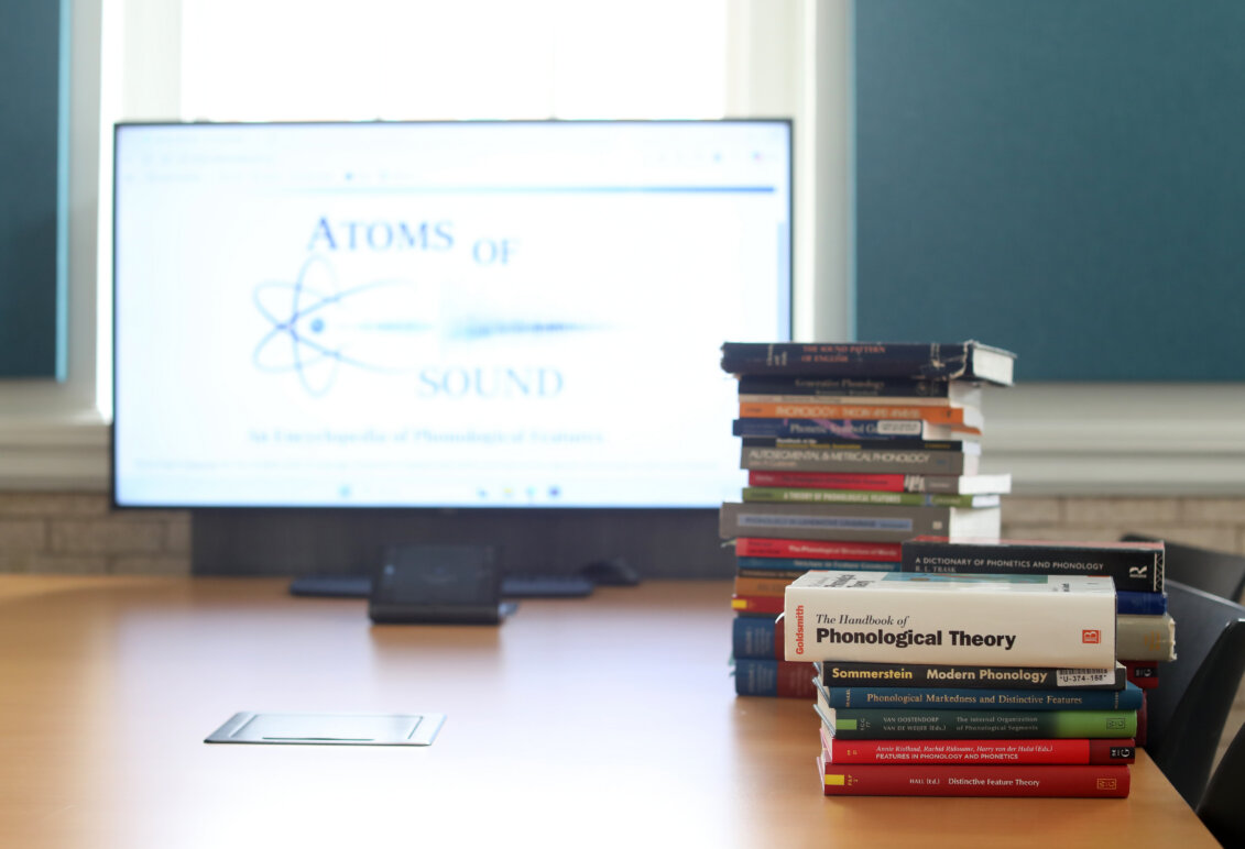 A stack of books sits in front of a laptop.
