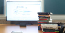 A stack of books sits in front of a laptop.
