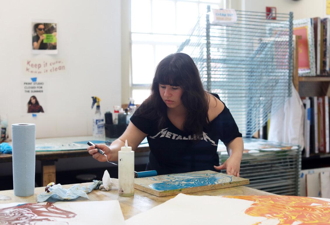 An art student brushes blue paint onto a linocut to create a relief printing.