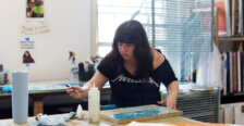 An art student brushes blue paint onto a linocut to create a relief printing.