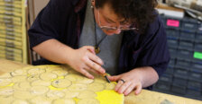 An art student carves away at a round, yellow piece of wood.