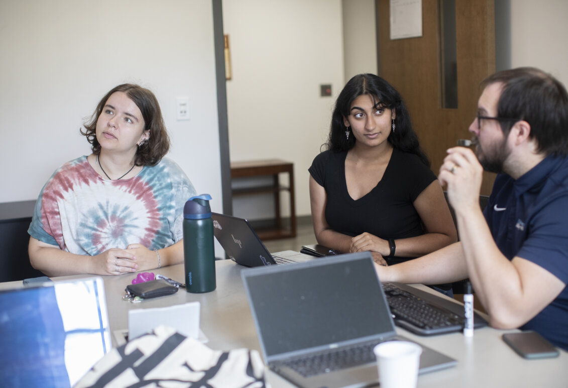 Two students and a professor sit around a table with laptops