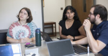 Two students and a professor sit around a table with laptops