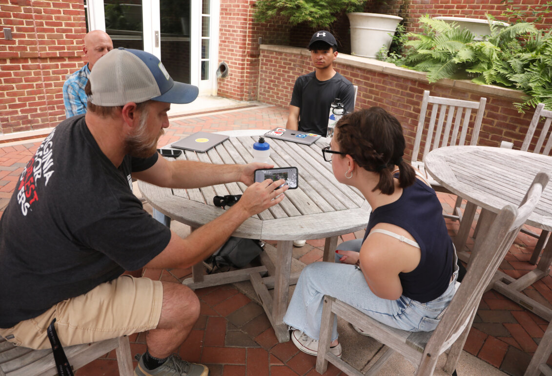 A Rappahannock River expert shows an iPhone photo to a UMW student, while another student and a professor look on.
