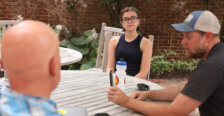 A student, a professor and another man sit at a table outside.