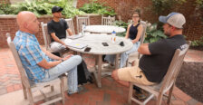 A professor, an expert on the Rappahannock River and two UMW students sit around a table near a brick building on campus.