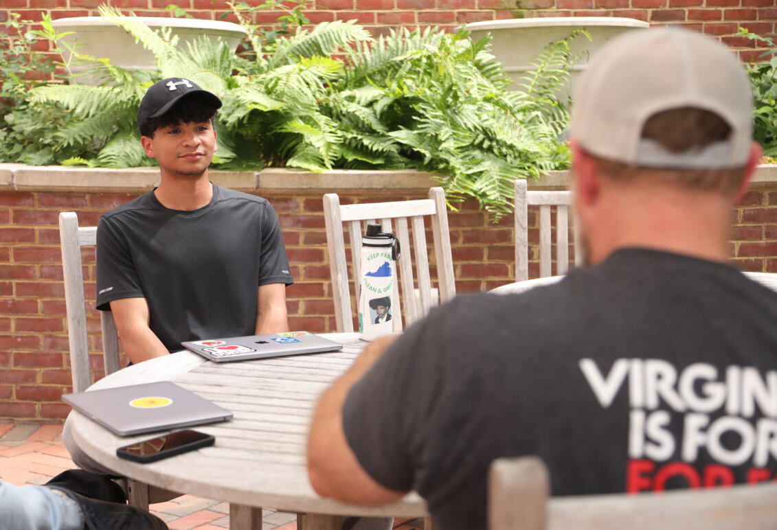 A student sits across an outside table from a man.